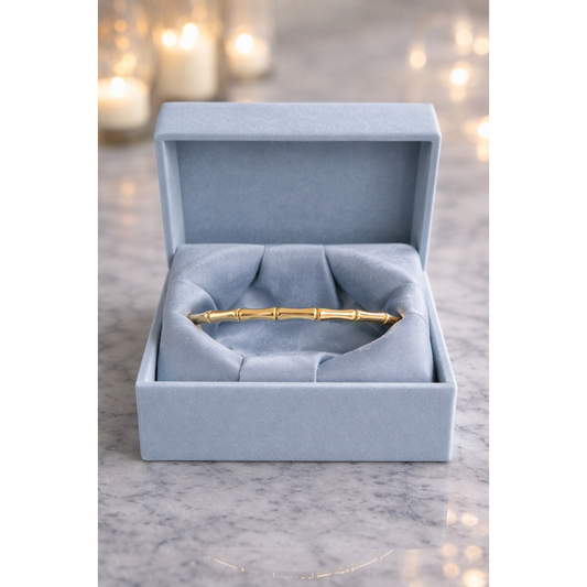Gold bamboo link bracelet with lock displayed in smokey blue velvet box on grey marble with blurred candles