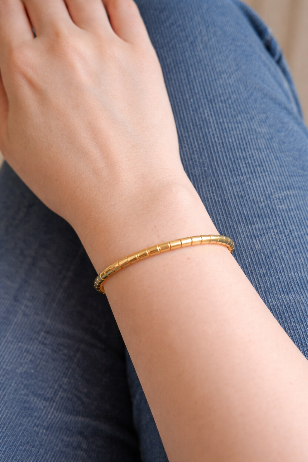 Gold segmented link bracelet with lock worn on feminine wrist resting on blue denim jeans in soft natural lighting