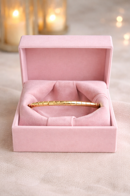 Gold segmented link bracelet with lock displayed in soft pink velvet box on marble with blurred candles 