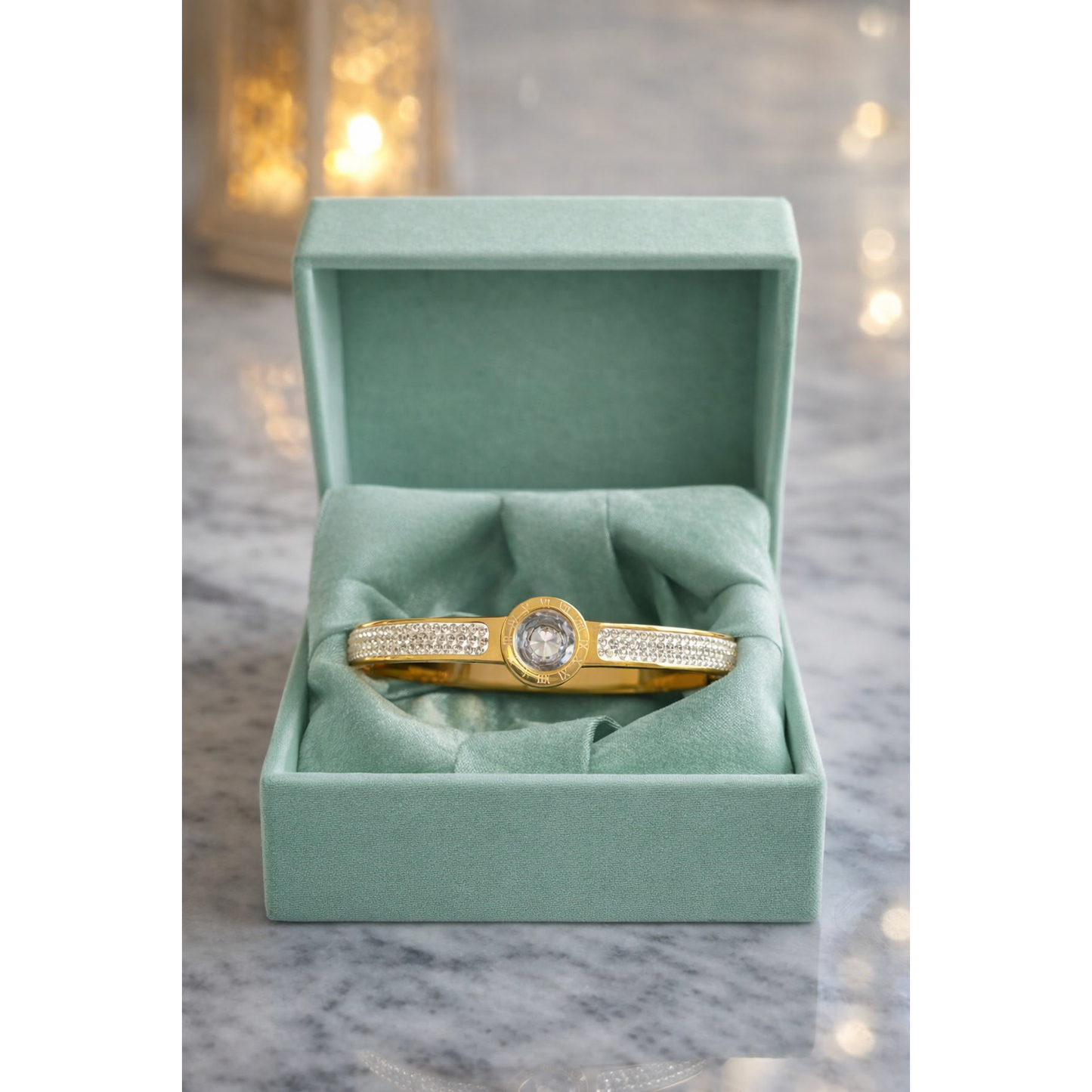 Gold Roman dial crystal bracelet with lock displayed in pastel green velvet box on marble surface