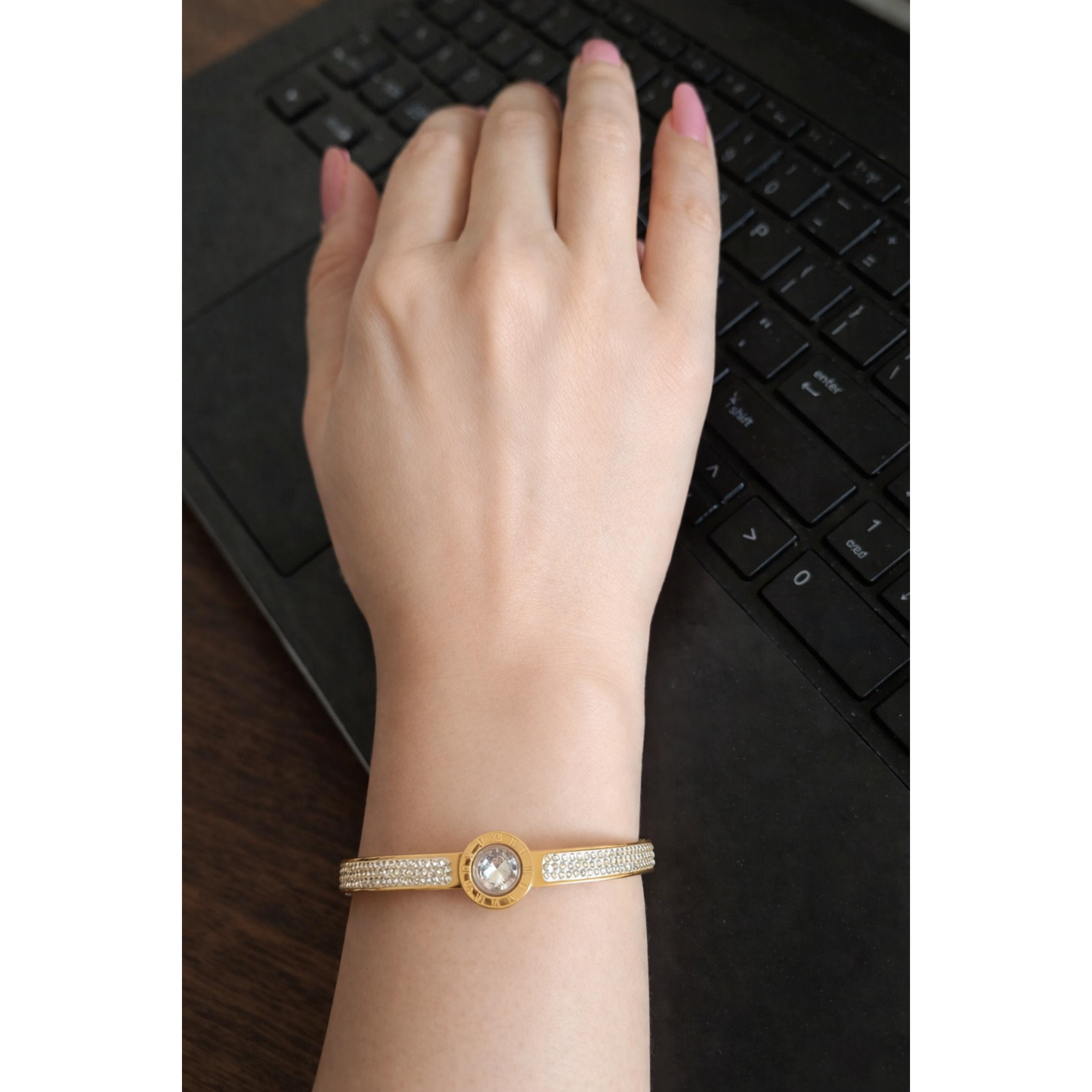 Gold Roman dial crystal bracelet with lock worn on feminine hand with pink nails on laptop workspace