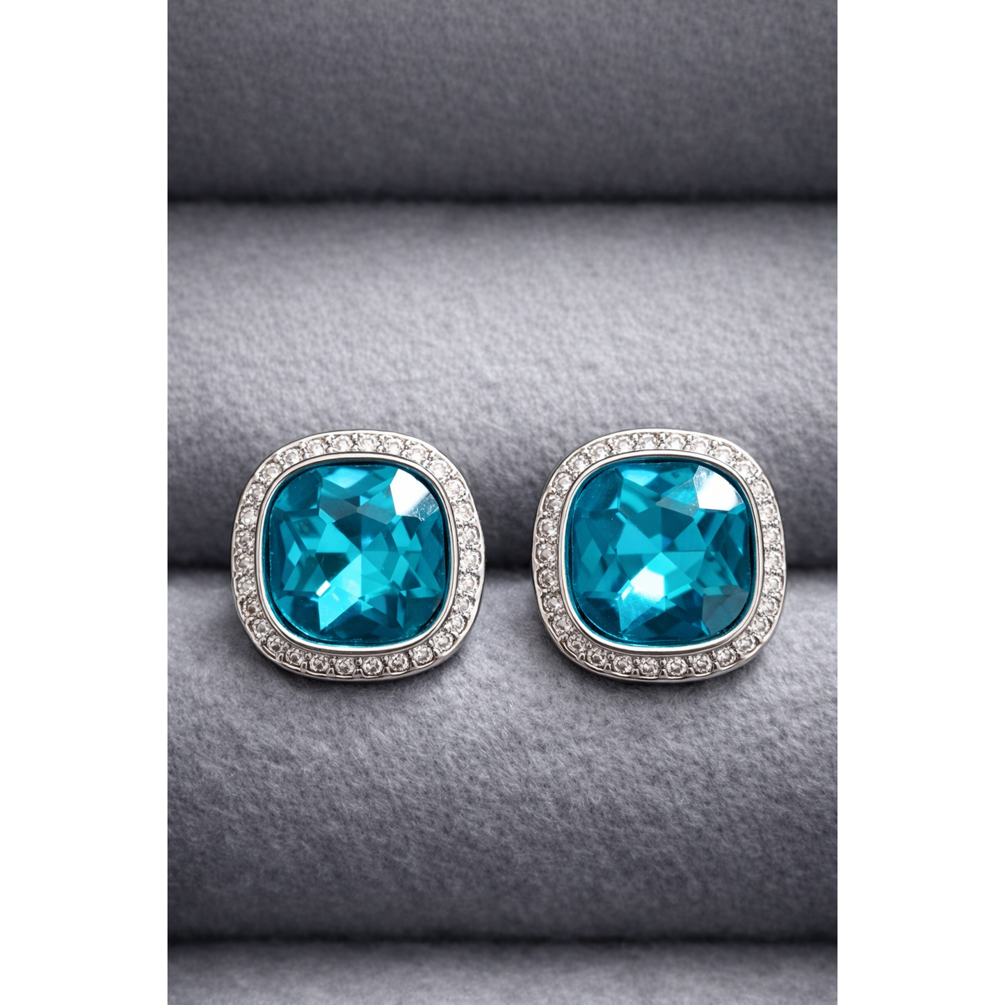 Pair of silver cushion-cut turquoise crystal studs with surrounding halo crystals photographed on grey velvet.