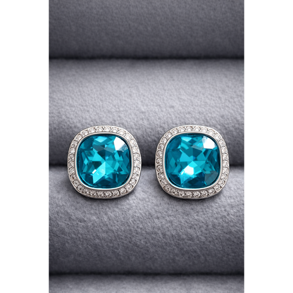 Pair of silver cushion-cut turquoise crystal studs with surrounding halo crystals photographed on grey velvet.