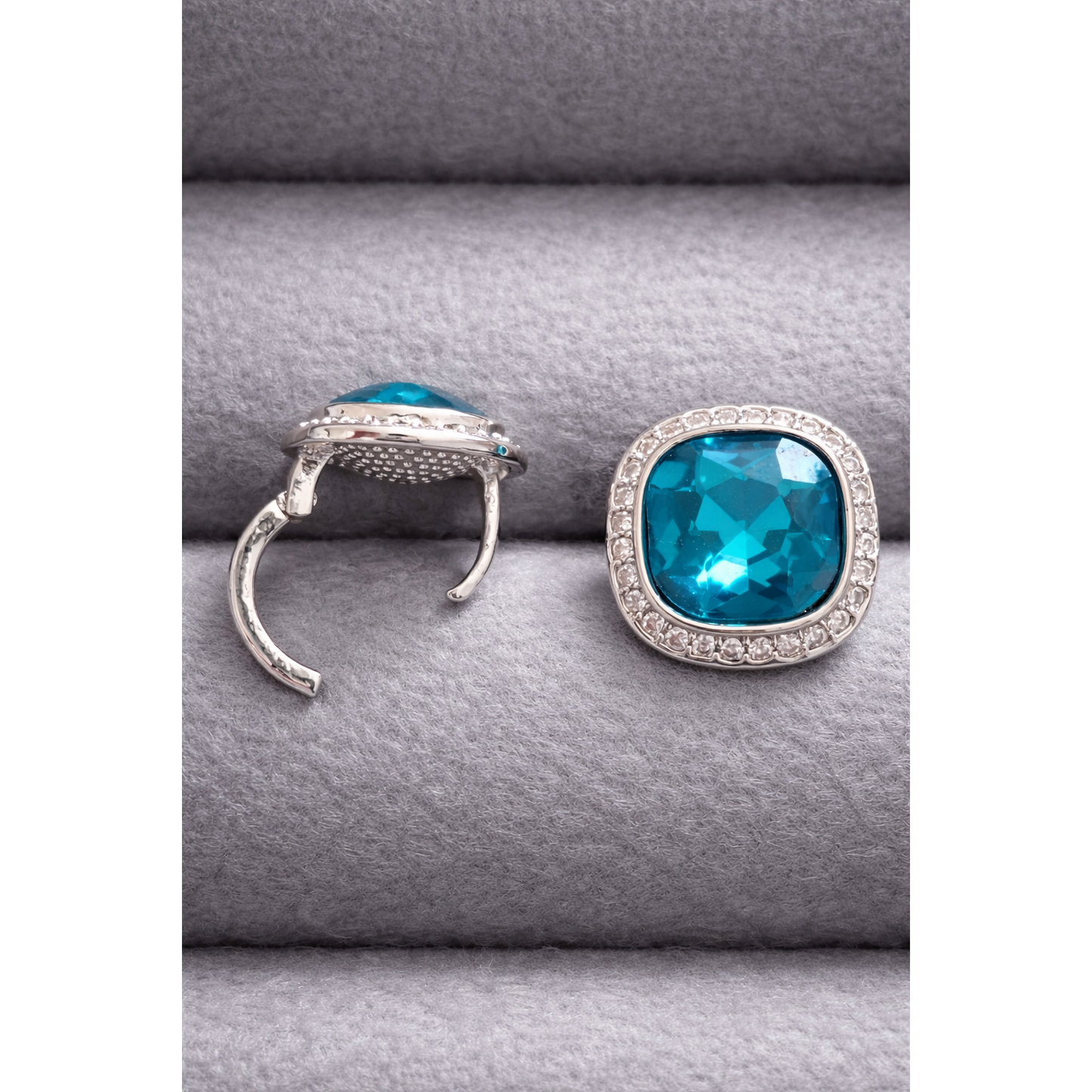 Silver cushion-cut turquoise crystal stud earring shown in side and front position with halo stones on grey velvet display.