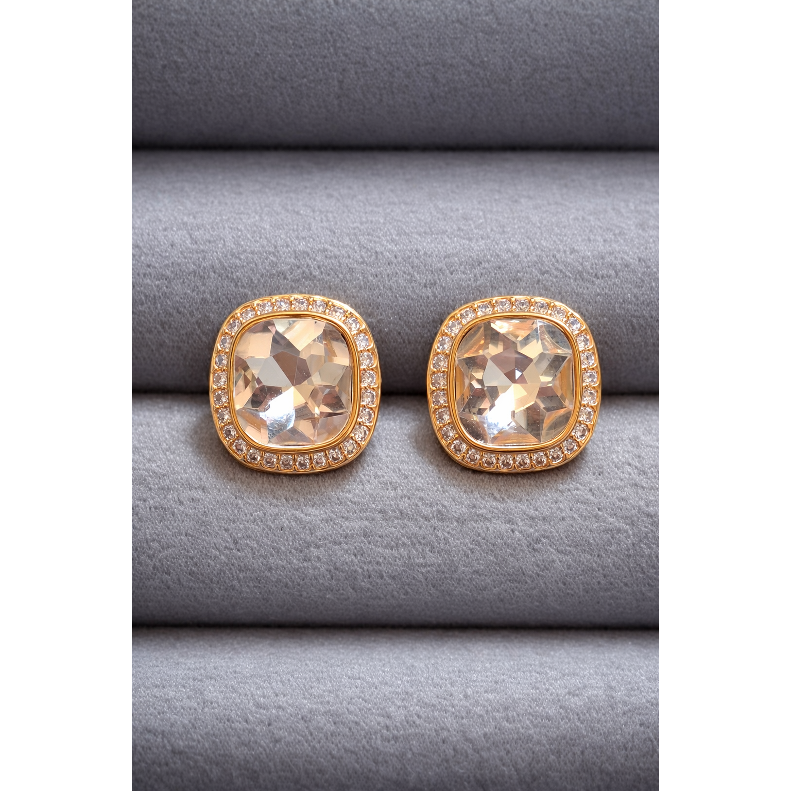 Pair of gold cushion-cut champagne crystal stud earrings with halo border displayed on grey velvet.
