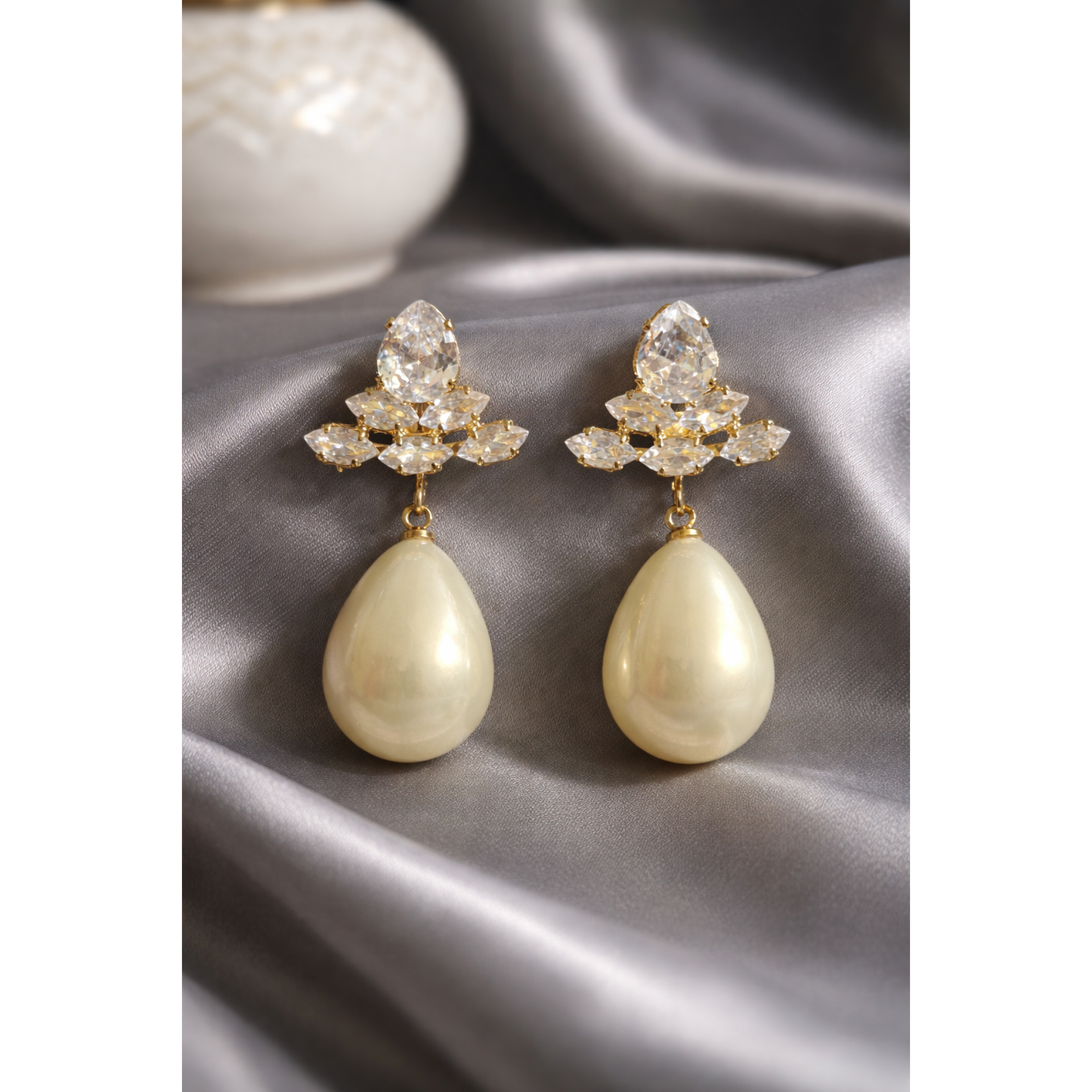 Pearl white teardrop crystal earrings displayed on grey satin with gold-tone crystal cluster