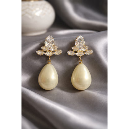 Pearl white teardrop crystal earrings displayed on grey satin with gold-tone crystal cluster