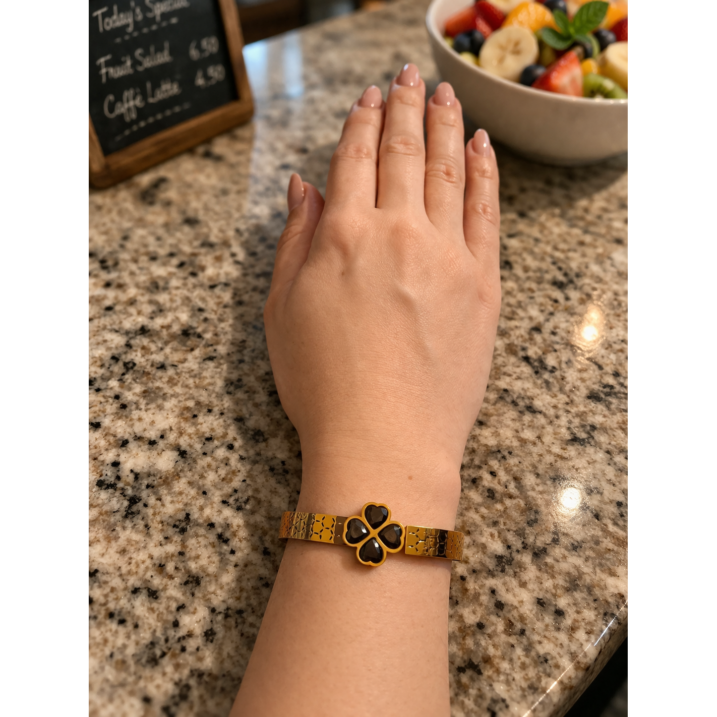 Gold clover bracelet with black stones worn on wrist on café counter