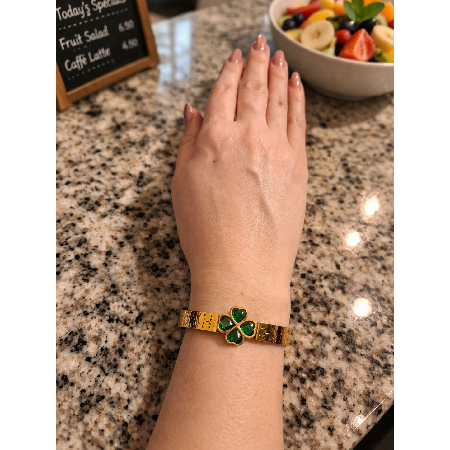 Gold clover bracelet with green stones worn on wrist on café counter