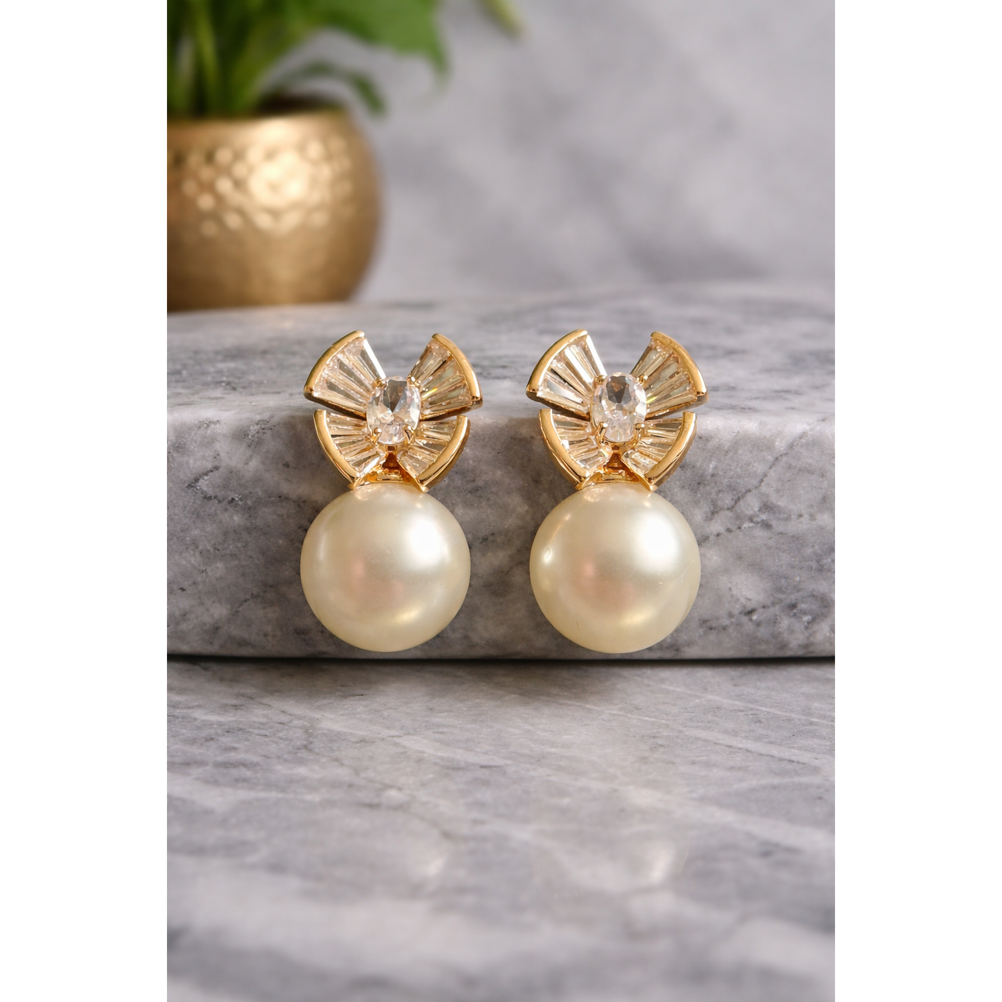 Gold-tone crystal fan pearl drop earrings displayed on grey marble with blurred golden vase