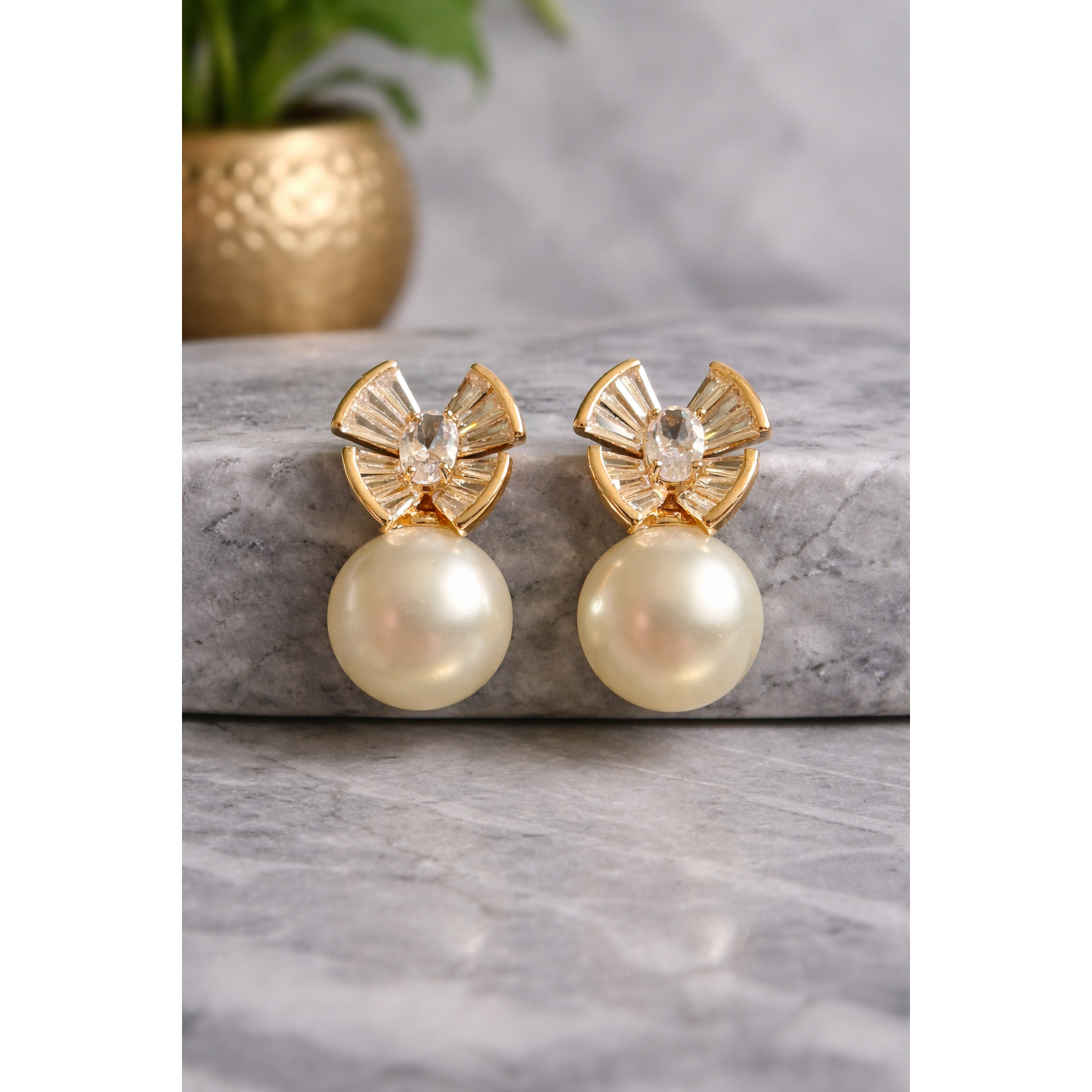 Gold-tone crystal fan pearl drop earrings displayed on grey marble with blurred golden vase
