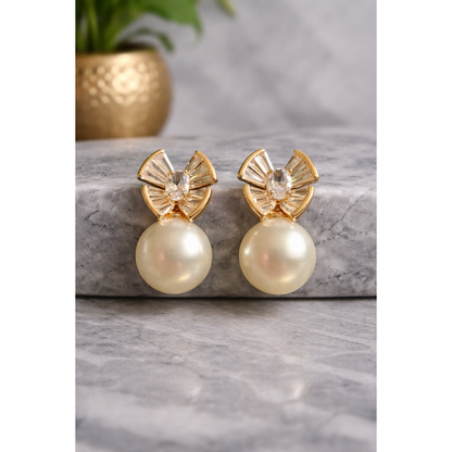 Gold-tone crystal fan pearl drop earrings displayed on grey marble with blurred golden vase