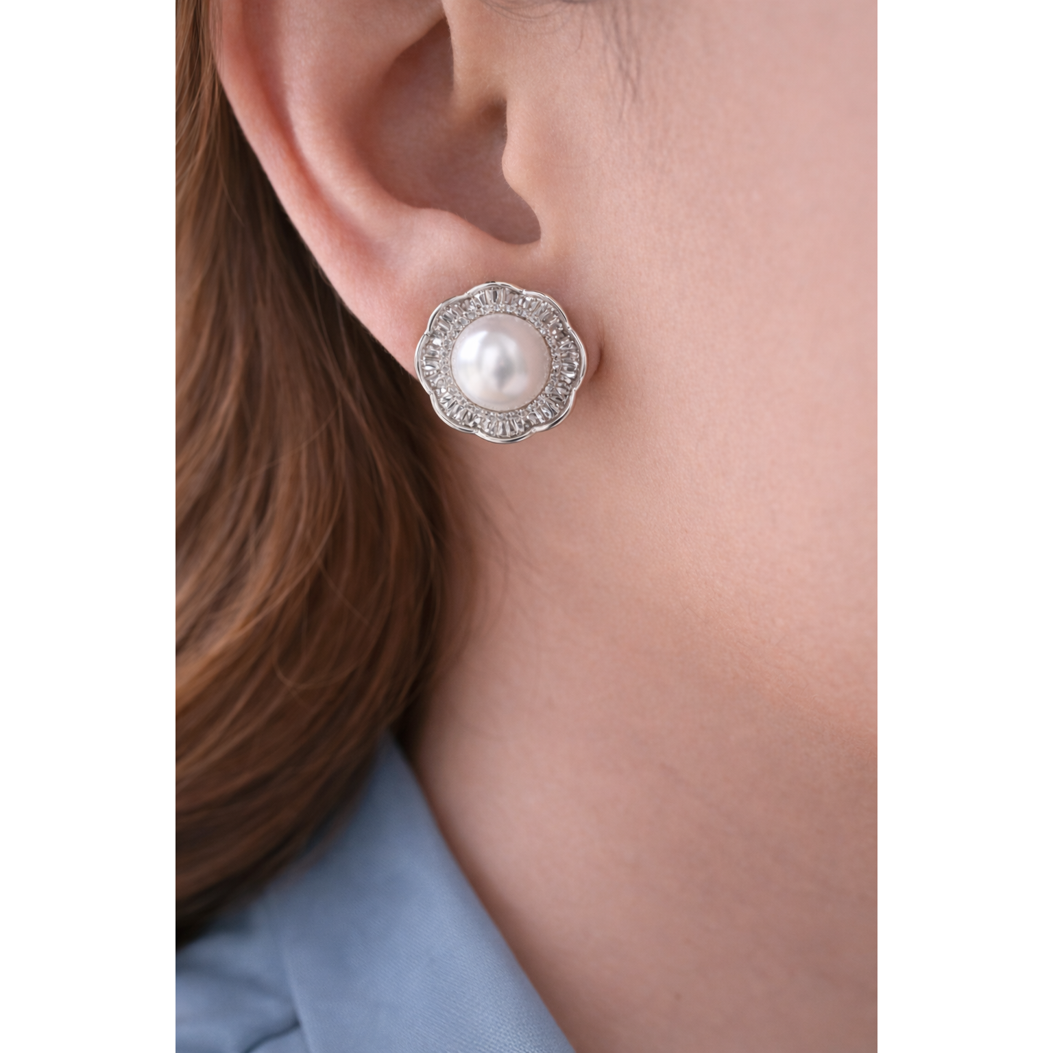 Silver floral halo pearl stud earrings worn on model with smoke blue shirt close-up