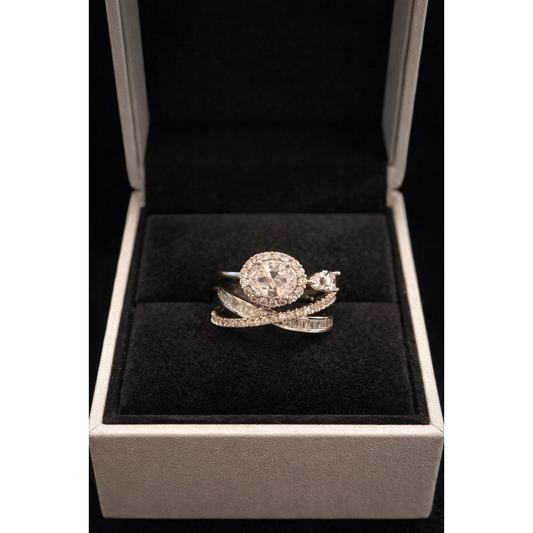 Oval halo crystal ring displayed inside luxury jewelry box with black velvet interior, showing layered baguette-style and pavé stone band in silver metal