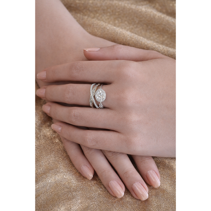 Oval halo crystal ring worn on female hand with nude manicure over golden shimmer fabric, featuring layered baguette-style and pavé silver metal band