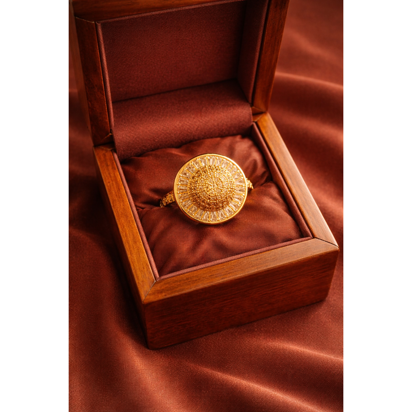 Gold halo statement ring with pavé dome center and baguette-cut stone frame displayed in a wooden jewelry box on rust satin background.