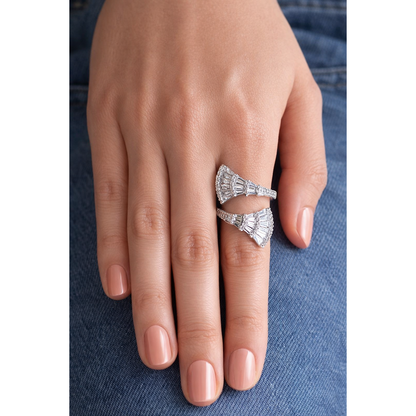 Silver tone open wrap fan-shaped baguette statement ring worn on female hand with peach pink nails against blue denim background