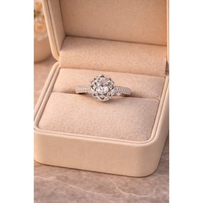 Silver round halo center stone ring displayed inside cream jewelry box with soft floral background