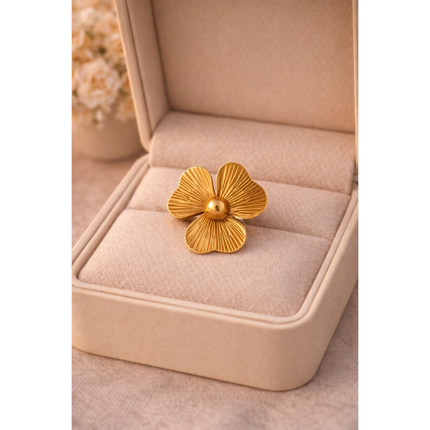 Gold floral statement ring placed inside cream jewelry box with soft blurred flowers in background