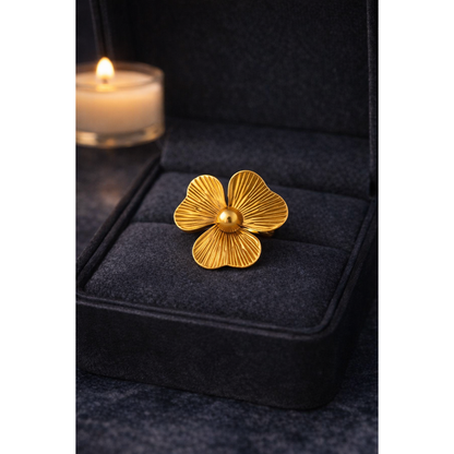 Gold flower statement ring displayed inside grey velvet jewelry box with blurred candle background and warm lighting