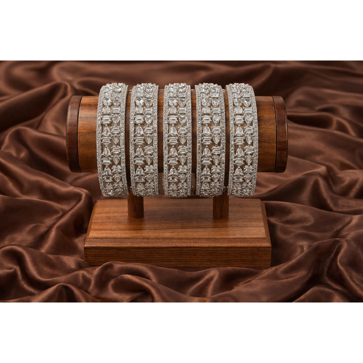 Silver crystal bangles displayed on wooden stand over brown satin fabric highlighting intricate pear and baguette stone setting