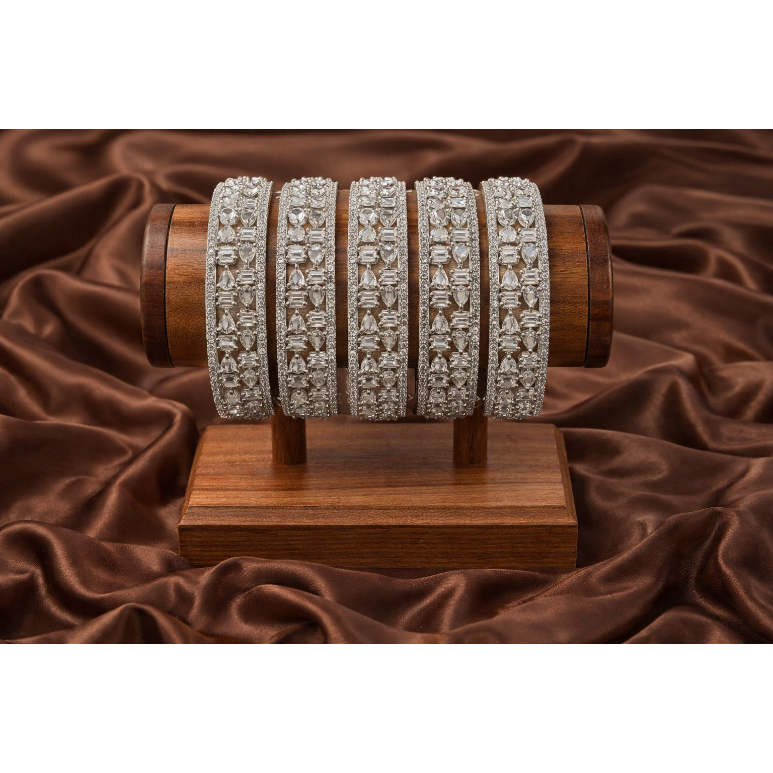 Silver crystal bangles displayed on wooden stand over brown satin fabric highlighting intricate pear and baguette stone setting