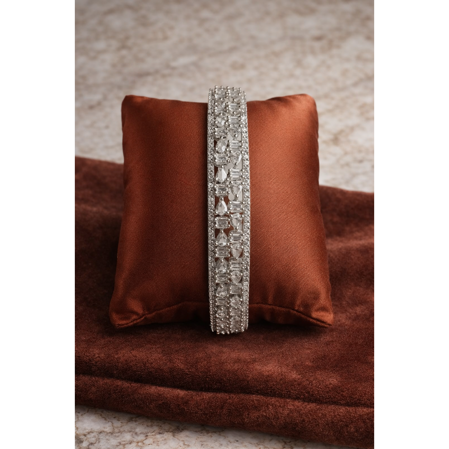 Silver crystal bangle placed on rust brown satin cushion with pear and baguette cut stones in detailed geometric design