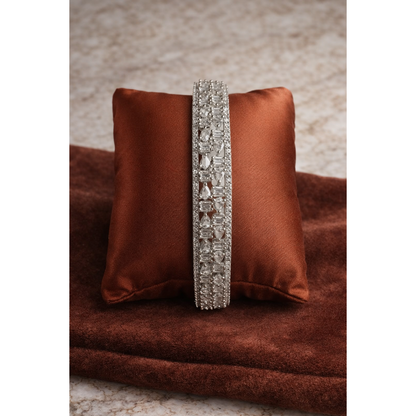 Silver crystal bangle placed on rust brown satin cushion with pear and baguette cut stones in detailed geometric design