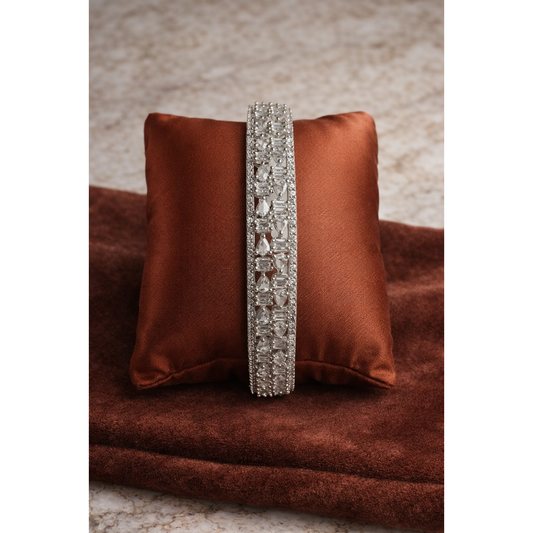 Silver crystal bangle placed on rust brown satin cushion with pear and baguette cut stones in detailed geometric design
