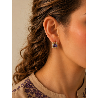Woman wearing gold-tone cushion stud earrings with zircon halo in royal purple stone variant