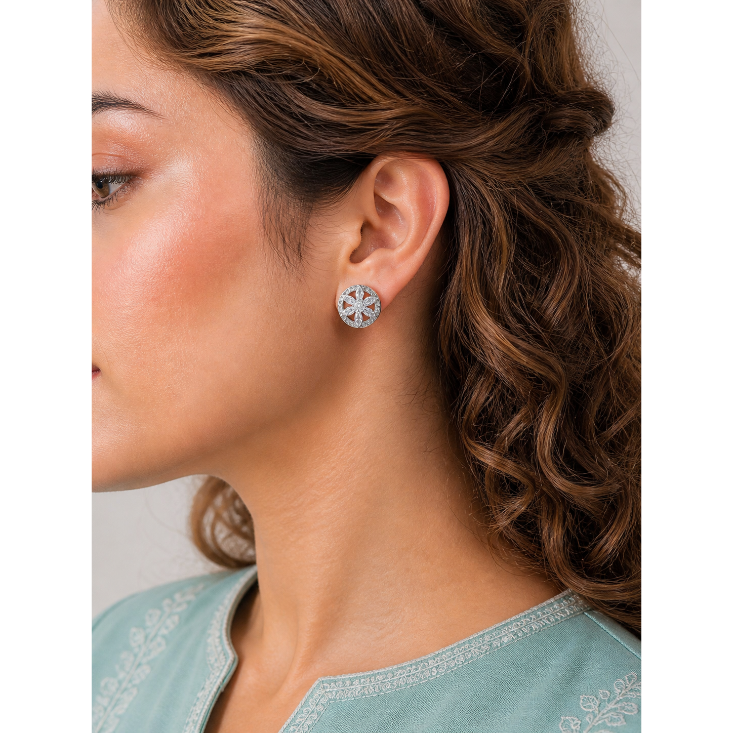 Close-up of a woman wearing silver floral earrings with a neutral background
