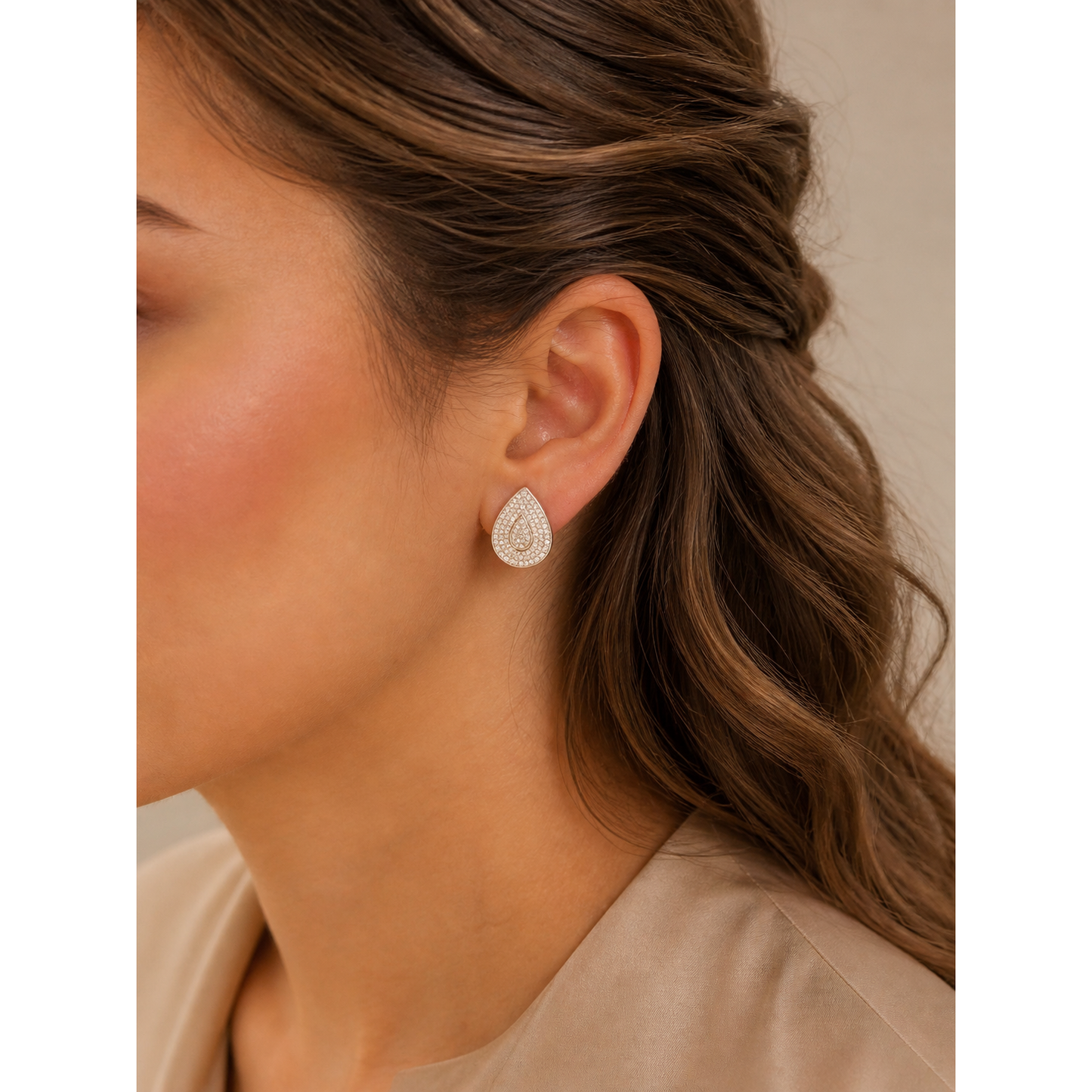 Silver teardrop crystal stud earrings worn on ear with brown wavy hair and soft makeup close-up