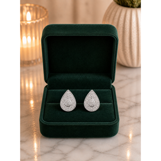 Silver pavé teardrop stud earrings displayed in forest green velvet jewelry box on marble surface with candle light