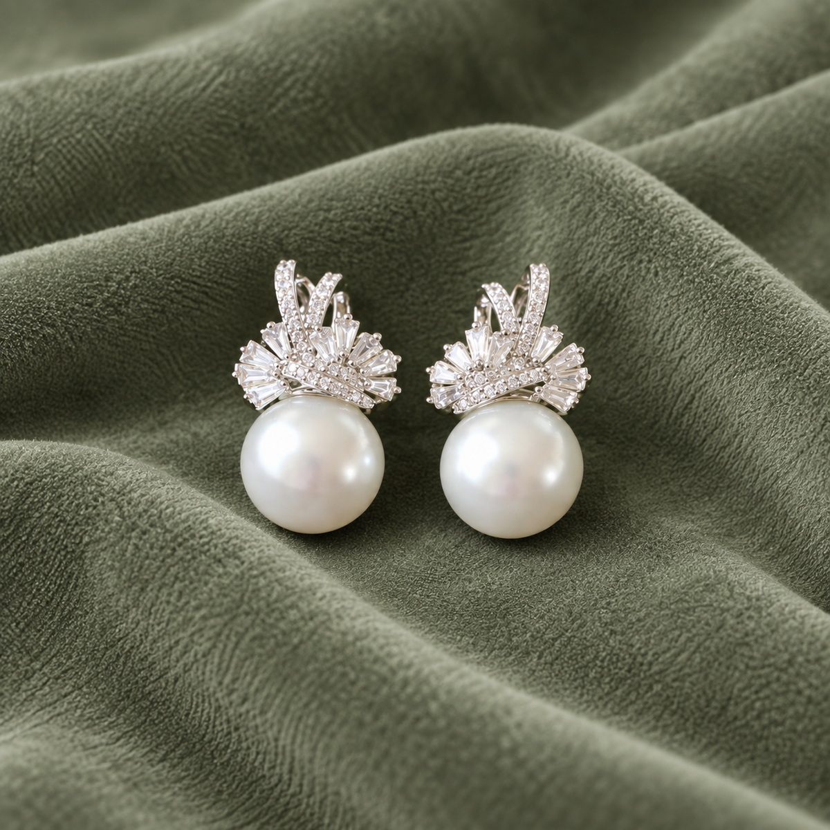 Pair of Gilded Fan Pearl Drop earrings in gold with clear baguette zircons and round pearl drops displayed on fabric.