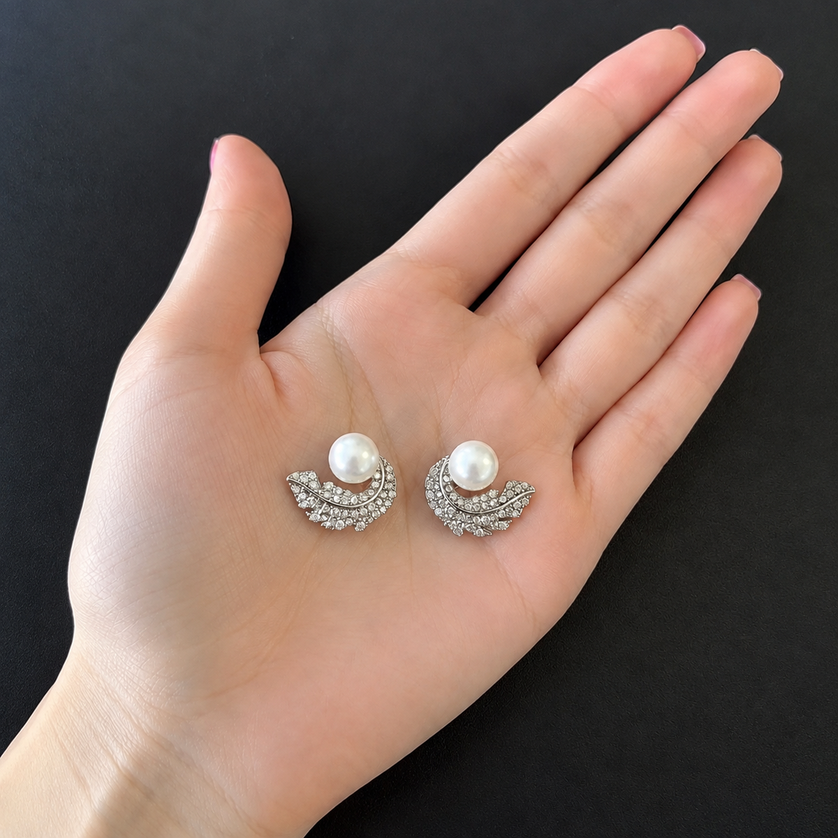 Swan Arc Studs featuring round white pearls with sweeping silver-tone swan-inspired arcs embellished with clear zircon displayed on a hand