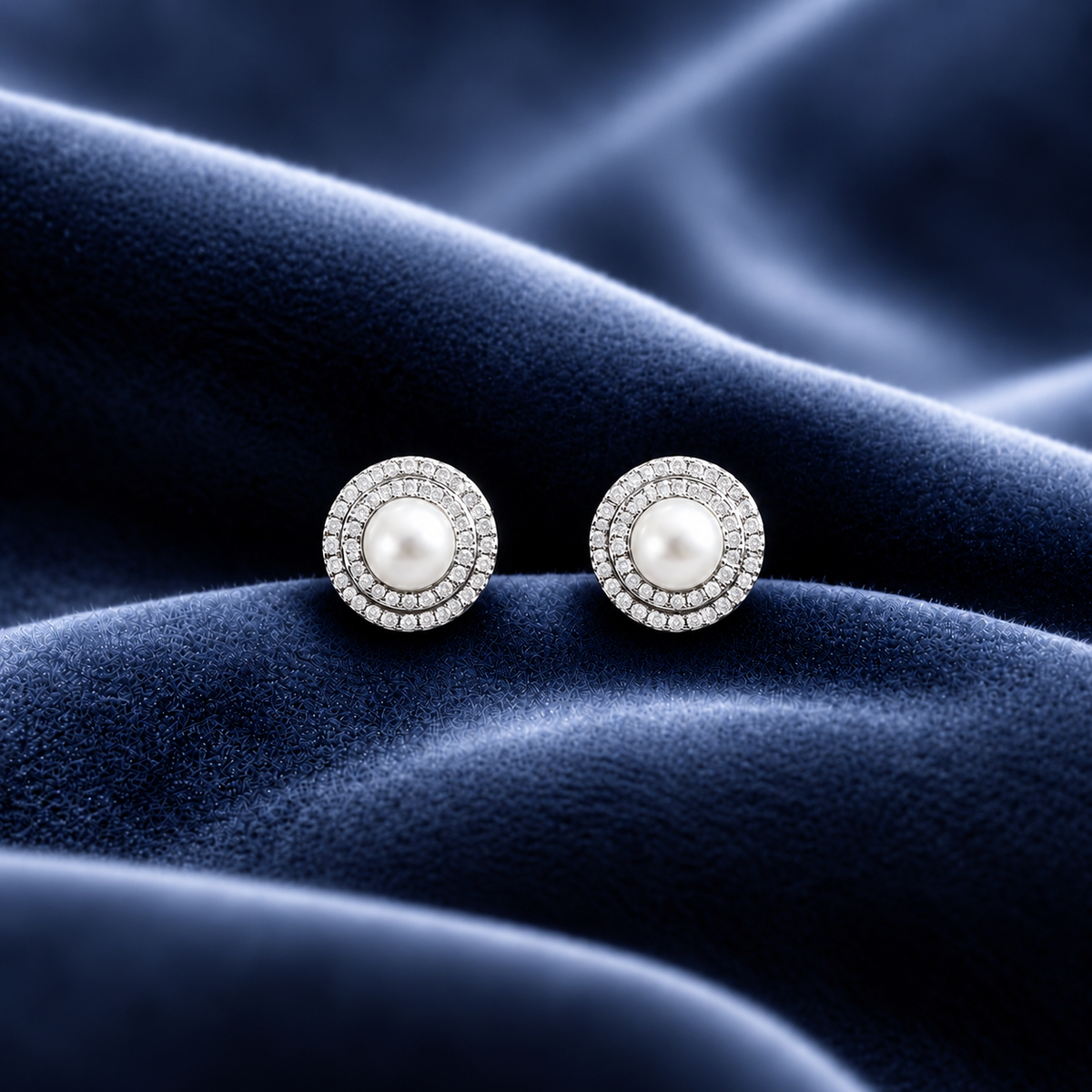 Pearl Meridian round stud earrings with white pearl centres and double rows of clear zircon stones, displayed on deep navy velvet.