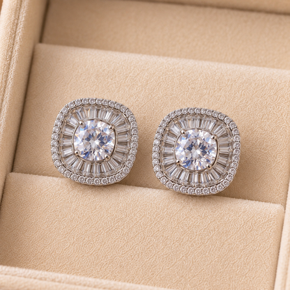 Close-up of cushion-shaped stud earrings featuring a round clear centre stone surrounded by radiating baguette-cut and tiny clear zircons.
