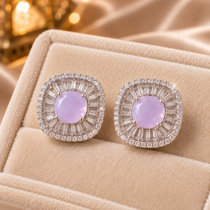 Close-up of cushion-shaped stud earrings featuring a round pink centre stone surrounded by radiating baguette-cut and tiny clear zircons.