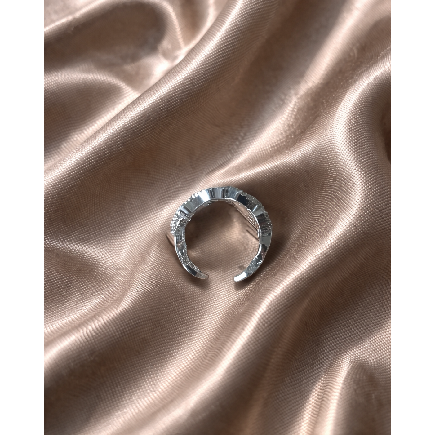 Silver textured open band ring placed on light brown satin fabric with soft folds