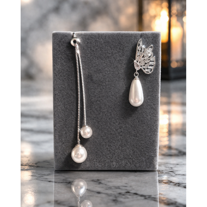 Silver butterfly pearl drop earrings with pearl chain detail displayed on fine grey velvet stand with blurred lantern background