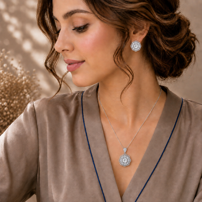 A woman wearing a silver-toned circular pendant necklace and matching earring, styled with a taupe satin robe.