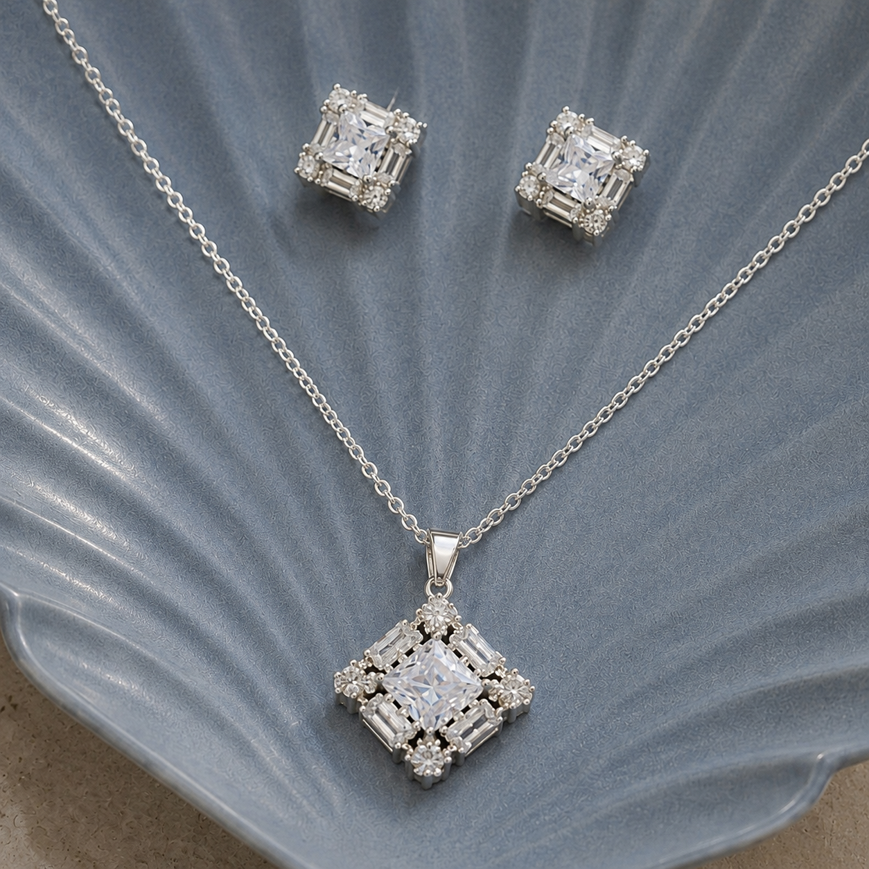 Facet Grid S925 silver earrings and pendant set with square clear stones and baguette-style zircon detailing displayed on a grey shell-shaped plate