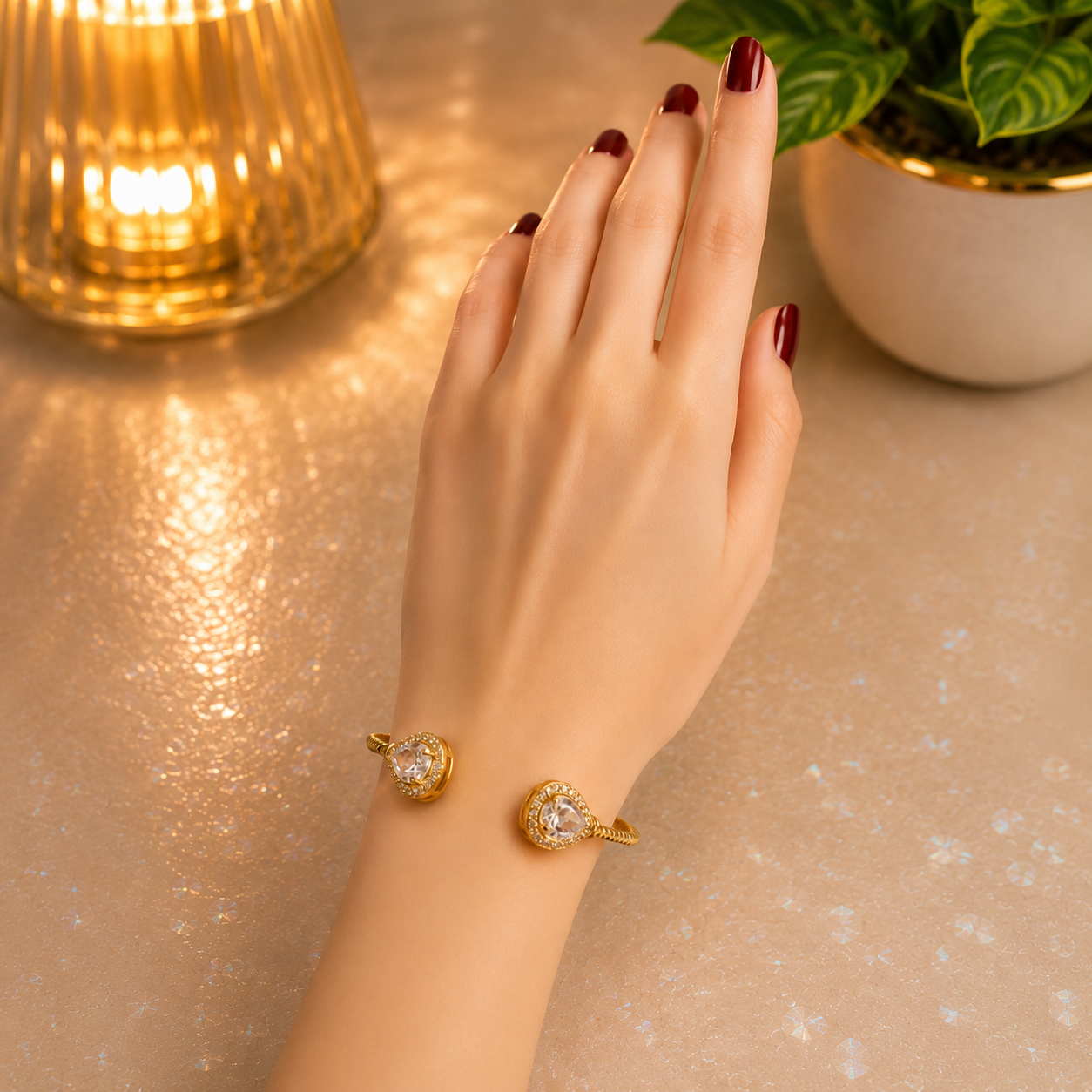 Gold open cuff bracelet with pear-cut crystal ends worn on a hand against a softly lit pearlescent background.