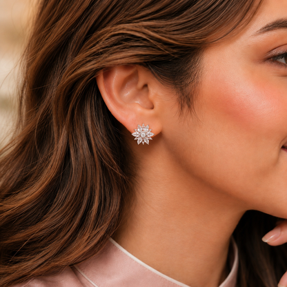 A close-up of a woman's ear wearing a small starburst stud earring made of clear gemstones in a silver-toned setting.