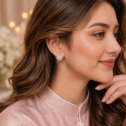 A close-up of a woman wearing a delicate silver-toned flower-shaped stud earring, dressed in a light pink satin traditional top with a high collar.