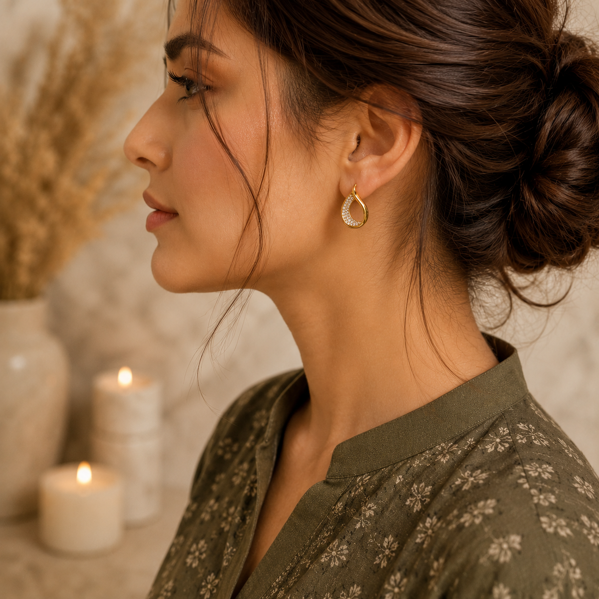 Woman wearing gold teardrop crystal earrings with an olive green printed shirt in a side-profile luxury portrait.