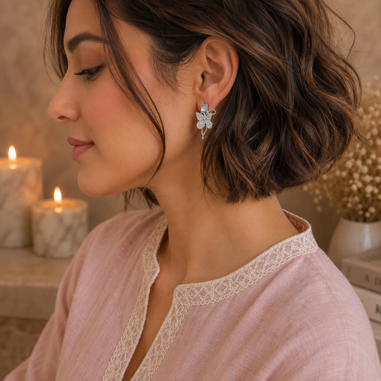 Woman wearing silver butterfly crystal earrings with a blush pink linen shirt in a side-profile luxury portrait.