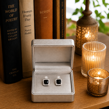 Silver-tone square halo zircon stud earrings with a cushion-cut black centre stone displayed inside a premium jewellery gift box with warm ambient lighting.