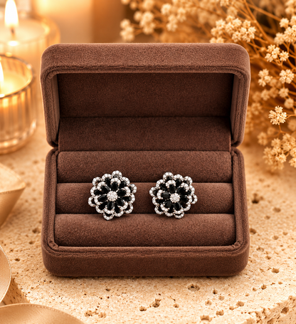 Midnight black floral crystal stud earrings displayed in luxury velvet jewelry box with warm decorative backdrop.