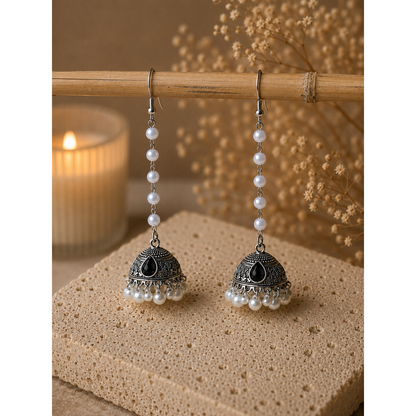 Pair of silver earrings with pearls on a wooden surface with a candle in the background